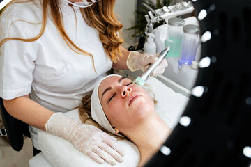 Fototapeta premium Young woman receiving modern facial low-voltage electrical treatment to stimulate elastin and collagen production for facial muscles improvement. Most popular face lifting treatment. Cosmetician work.