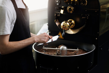 Young caucasian male barista managing coffee roasting process in factory, use tablet computer