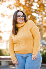 Smiling woman 35-39 year old wearing eye glasses and knitted yellow sweater over yellow leaves...