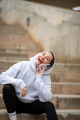 Obraz premium Laughing young woman in hoodie talking on mobile phone outdoors
