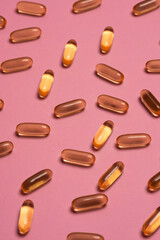 Top view composition of orange vitamin pills scattered on pink background in light studio