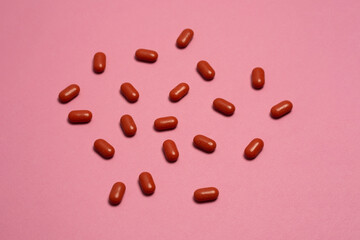 Many red coated pills randomly scattered on pastel pink background. Concept of medicine, pharmacy, vitamins, supplements, healthcare and treatment. Modern minimal flat lay.
