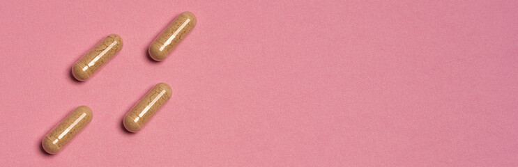 Four natural herbal supplement capsules on pastel pink background. Concept of vitamins, nutrition, alternative medicine, wellness and healthy lifestyle. Minimal modern flat lay.