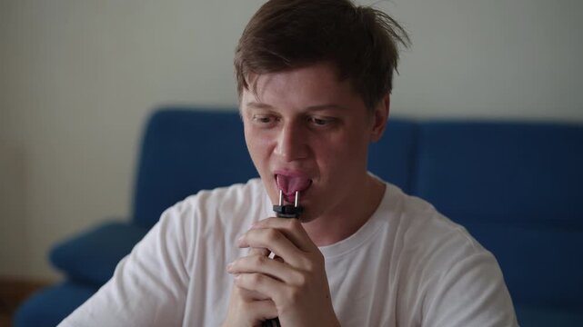 Portrait of unresponsive man carelessly licking power plug, demonstrating dangerous lack of awareness about electric shock risk, symbolizing foolish behavior and unsafe practices with electricity.