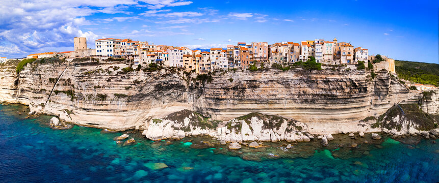 France Corsica Bonifacio village aerial 8K. Ancient houses hanging over limestone white cliffs with turquoise sea water. Scenic Mediterranean travel destination. World Print 8000px summer scenery