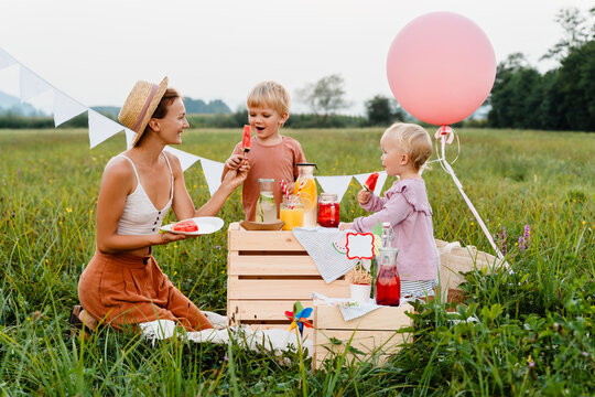 Mother with little children having imaginary picnic in meadow. Kids playing with her mom in nature.