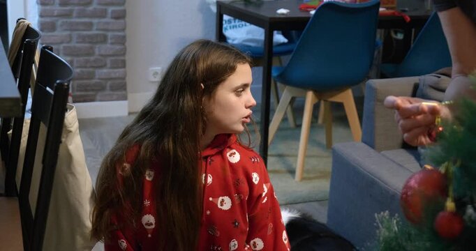 Girl watches her mother decorate the Christmas tree, close-up of mother's hands on the tree.