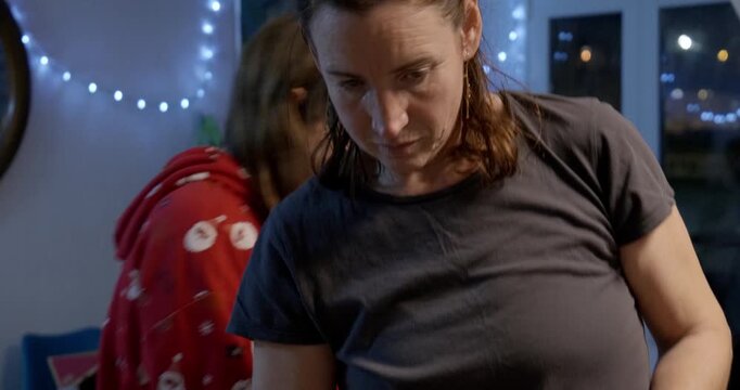 Girl watches her mother decorate the Christmas tree, crosses paths with her. Night.