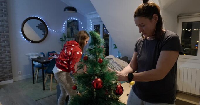 Mother and daughter decorating the Christmas tree at home in the evening. Wide shot.