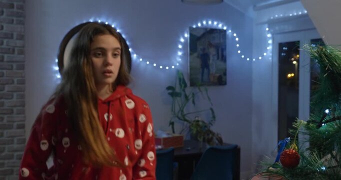 Close-up of a girl wearing red Christmas clothes, putting decorations on the Christmas tree. She steps back to look at it.