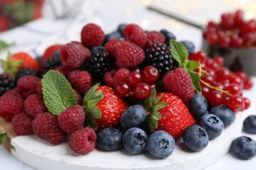 Different ripe berries and mint leaves on white table, closeup