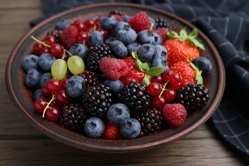 Different ripe berries in bowl on wooden table, closeup
