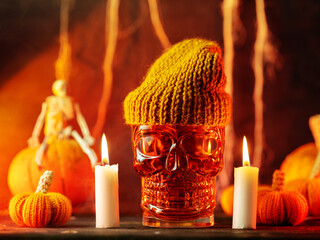 Halloween cocktail in a skull glass. Burning candles and crocheted pumpkins.