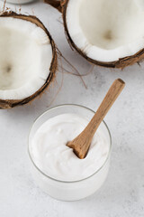 Fresh coconut yogurt in a glass jar with a wooden spoon and coconuts. Vegan yogurt, lactose-free.