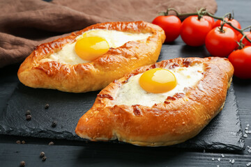 Tasty khachapuri with cheese, eggs, tomatoes and spices on black wooden table, closeup