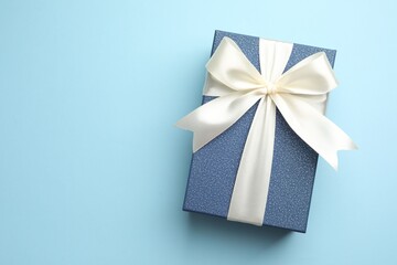 Gift box with beautiful bow on light blue background, top view. Space for text