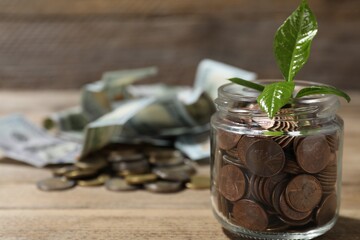 Glass jar with coins, sprout and banknotes on wooden table, closeup