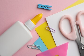 Glue in bottle, color paper and other stationery on pink background, flat lay