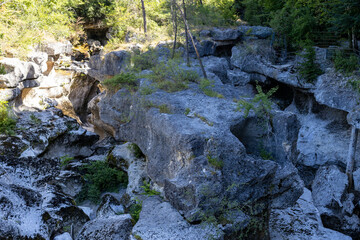 Sunlit natural rock formations in a scenic gorge, highlighting geological erosion and sparse vegetation.