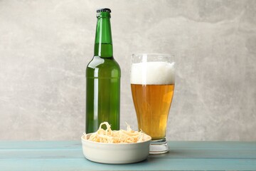 Dried squid shavings and beer on light blue wooden table against grey background, closeup