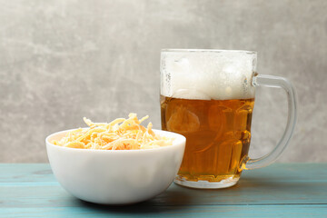 Dried squid shavings and glass mug of beer on light blue wooden table against grey background, closeup