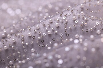 Detailed close-up of pearl, ice grey lace with sequins and beads on delicate mesh, creating a shimmering texture perfect for fashion, couture, and luxury fabric backgrounds