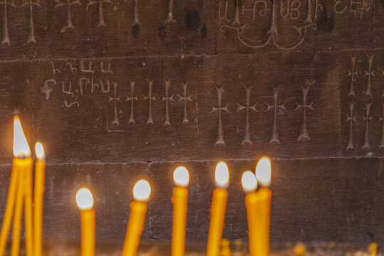 View of flickering candlelight dances against the ancient stone, illuminating carved crosses and Armenian script, creating a warm glow in Noravank Monastery, Vayots Dzor Province, Armenia.