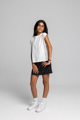 Cheerful teen girl standing in white t-shirt and black denim skirt, trendy casual fashion studio portrait.