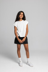 Charming teenage girl posing in casual white t-shirt and black skirt, full body studio shot with smile.