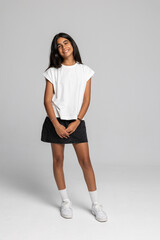 Charming teenage girl posing in casual white t-shirt and black skirt, full body studio shot with smile.