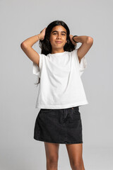Energetic teenage girl posing playfully with hands in hair, casual white t-shirt and denim skirt studio shot.