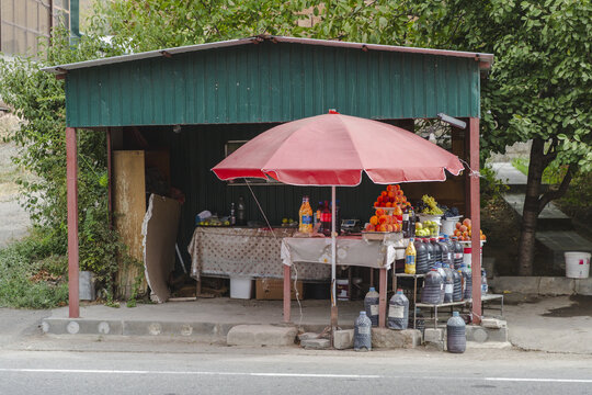 View of a roadside stall, shaded by a red umbrella, displays a colorful array of fruits and drinks in the Armenian countryside, Areni, Vayots Dzor Province, Armenia.