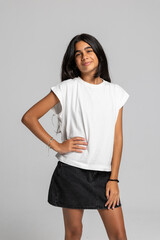 Teenage girl posing confidently in casual white t-shirt and black denim skirt, stylish fashion studio portrait.