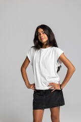 Teenage girl posing confidently in casual white t-shirt and black denim skirt, stylish fashion studio portrait.