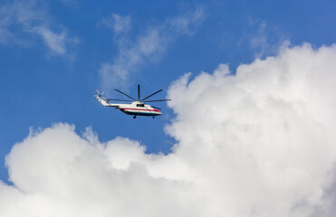 A helicopter flying against a backdrop of a clear blue sky and white clouds.