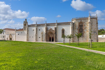 Fototapeta premium Historic Monastery of Jesus in Setúbal, Portugal, showcasing Gothic Manueline architecture, stone details, and peaceful green surroundings under blue sky.
