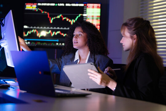Colleagues discuss stock market trends in a modern office setting during evening hours