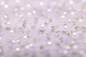 Close-up of elegant, off-white pearl lace fabric with delicate beads and sequins on fine mesh, creating a shimmering texture ideal for fashion, bridal, and luxury design concepts.