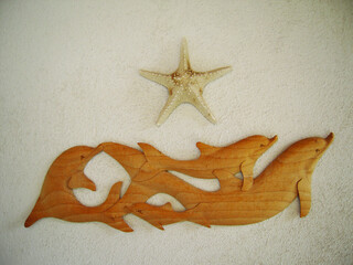 Wooden wall decoration featuring a pod of dolphins swimming together with a starfish above, mounted on a textured white surface, evoking a coastal and ocean theme.