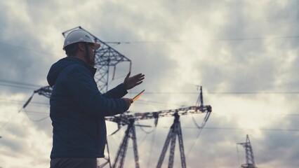 An engineer at a high voltage power plant works in a tablet at sunset in the sky, electrical energy design, industry concept, modern business technologies, an electrician reads a project on a gadget
