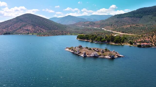 Aerial footage captures the tranquil beauty of Bafa Lake in Turkey, showcasing its deep blue waters, a picturesque island dotted with sparse vegetation, and the surrounding majestic mountains under a 