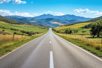 Naklejka premium Road stretching through vibrant fields and rolling mountains under a clear blue sky