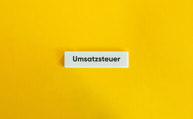 Umsatzsteuer Schriftzug auf weißem Kachelstein vor gelbem Hintergrund