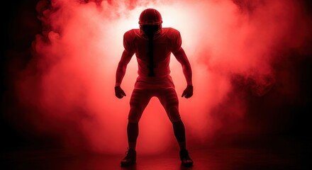 Dramatic silhouette of American football player standing in red smoke with helmet and full gear creating powerful energy and intensity in dark stadium background