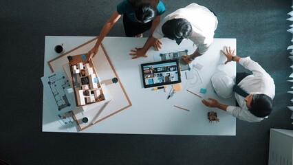 Top down view of architect engineer team discussing and point at tablet display construction at table with blueprint and house model at meeting. Diverse designer planning design house. Alimentation.