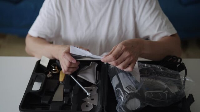 Man carefully reading technical instruction manual, learning to use new electric heat gun from toolbox, preparing for home improvement project or doing DIY task, close-up. Shooting in slow motion.