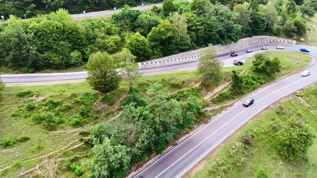 Mountain road with sharp turn in Romania. Vehicles drive along a sharp curved mountain road surrounded by dense green forest in Romania.