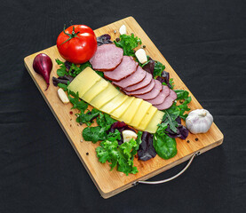 Set board with sliced cheese, ham, tomatoes and peppers, garlic and herbs. Healthy protein menu.
