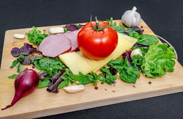 Set board with sliced cheese, ham, tomatoes and peppers, garlic and herbs. Healthy protein menu.