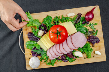 Female hands decorate set of cheese, ham and tomato with mixed salad leaves. Food decoration concept